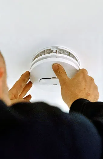 Electrician smoke testing a ceiling mounted photoelectric alarm in a Brisbane home
